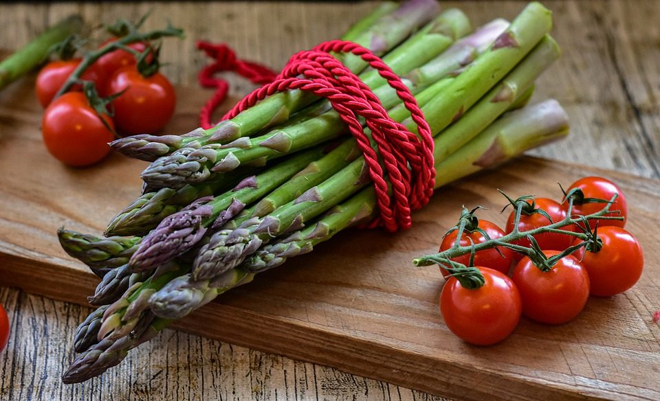 Bosje groene asperges en cherrytomaten op een snijplank